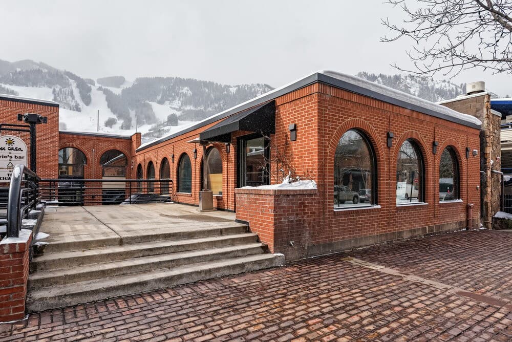 The brick, arched facade of 315 E. Hyman Ave in downtown Aspen, with Aspen Mountain behind it in winter